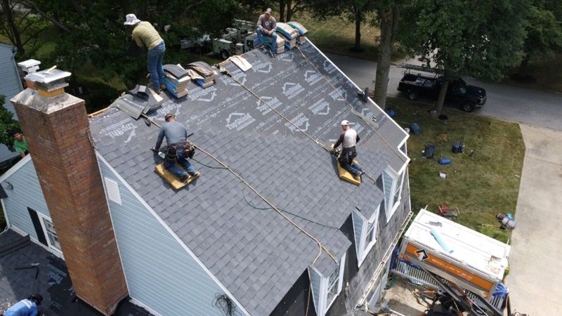 Wheeler crew installing asphalt shingles over roof underlayment